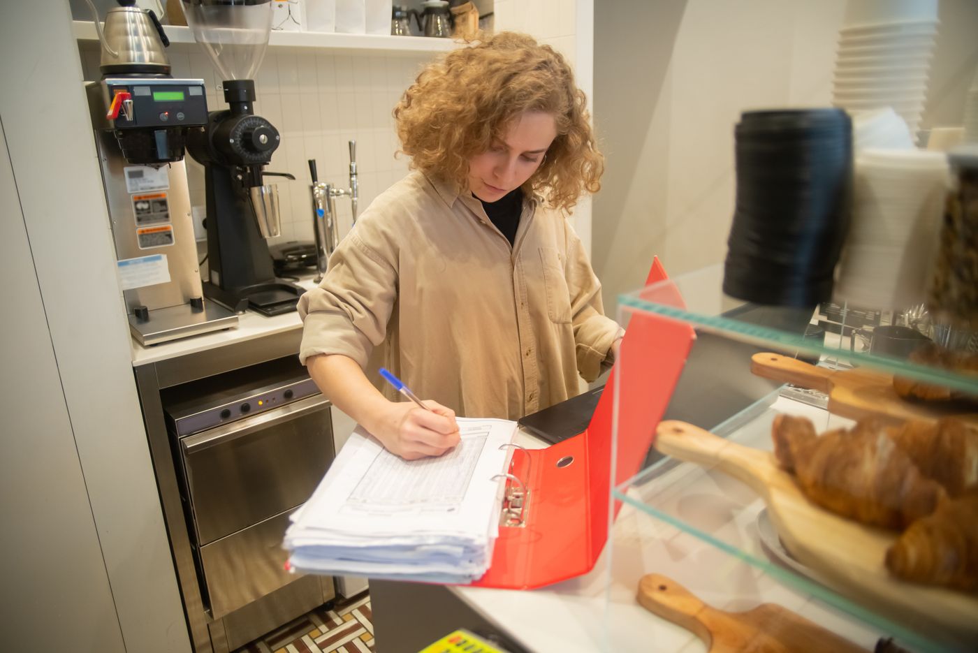 Uma trabalhadora de café a consultar registos atrás de um balcão de pastelaria em Portugal.